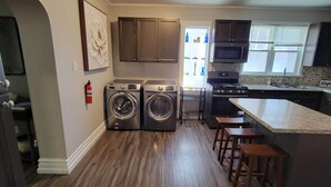A modern kitchen with built-in appliances, a central island with stools, and a large window providing natural light. - The Hideaway Walk to Falls W/D Sleeps 8 (Niagara Falls)