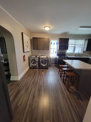A modern kitchen with built-in appliances, a central island with stools, and a large window providing natural light. - The Hideaway Walk to Falls W/D Sleeps 8 (Niagara Falls)