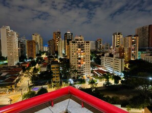 A cityscape at night with high-rise buildings and a red railing in the foreground. - Premium Flat - 500m from Ibirapuera Park: Comfort, swimming pool, free parking and leisure facilities. (São Paulo)