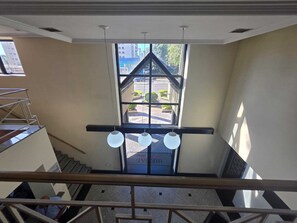 A view from a balcony overlooking a building entrance with a glass door, a metal staircase, and a hanging light fixture. - Premium Flat - 500m from Ibirapuera Park: Comfort, swimming pool, free parking and leisure facilities. (São Paulo)