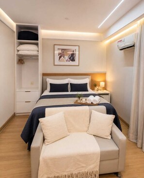 A hotel room with a bed, bedside tables, a wardrobe, a seating area, and a wall-mounted air conditioner. - Premium Apartment - 500 meters from Ibirapuera Park: Comfort, swimming pool, free parking, and recreational activities. (São Paulo)