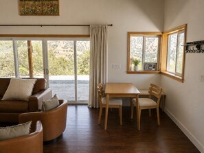 Ein Zimmer mit braunem Ledersofa, einem Holztisch mit Stühlen, einem großen Fenster mit Blick auf Grünflächen und einem an der Decke befestigten Kunstwerk.