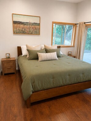 Ein Schlafzimmer mit einem großen Bett, Holznachttischen, einem Fenster mit Vorhängen und einem Landschaftsbild an der Wand.