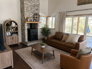 Ein Wohnzimmer mit Kamin aus Stein, einem braunen Ledersofa, einem Couchtisch aus Holz und einem Fernseher auf einem Holzständer.