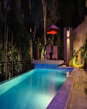 Una piscina con borde de azulejos, rodeada de una valla y vegetación.