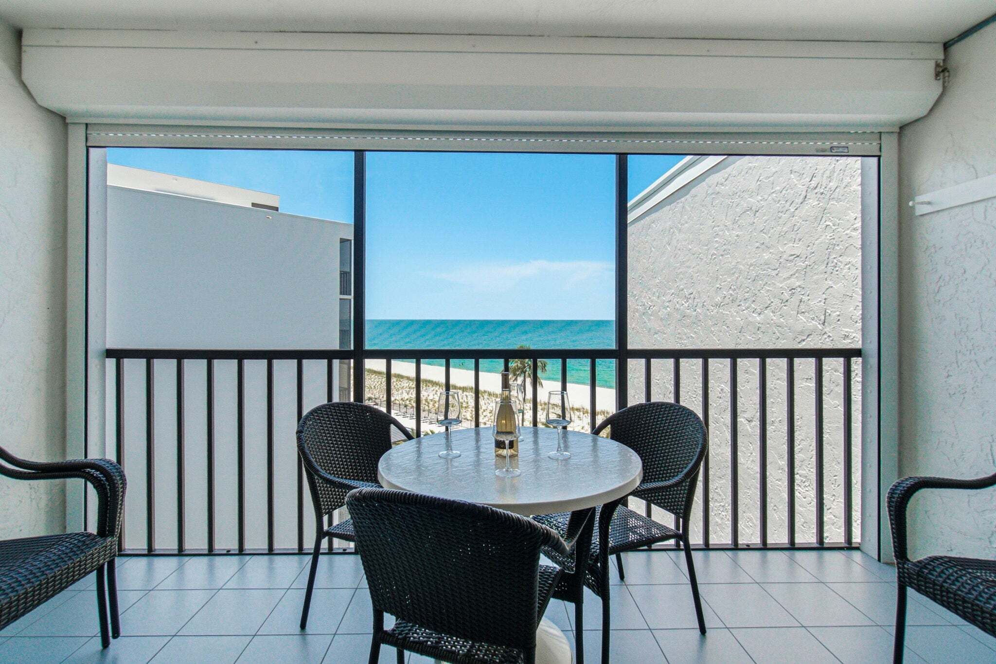 A balcony with a table and chairs, overlooking a beach.