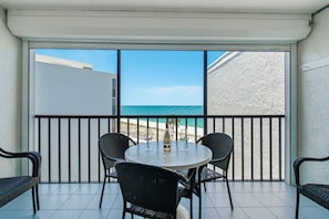 A balcony with a table and chairs, overlooking a beach. - Beachfront 2BR Condo with Gulf Views, Screened Lanai & Pickleball | Sleeps 4 (Bonita Springs)