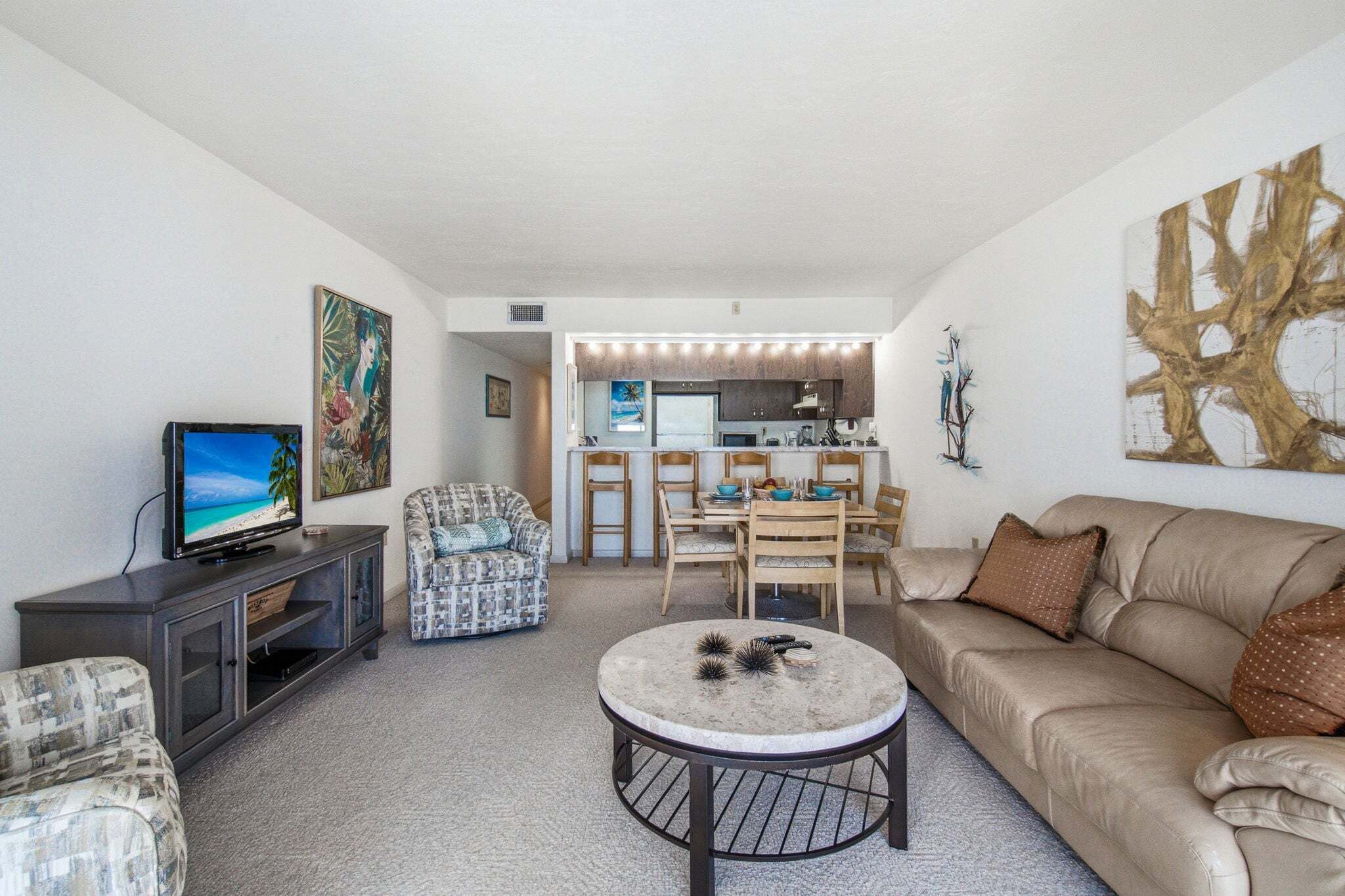 A living room with a television, a patterned armchair, a round coffee table, a sofa, and a dining area with chairs and a table.