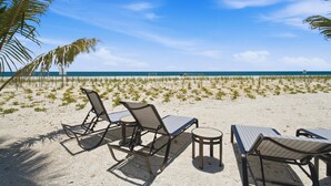 Ein Strand mit Liegestühlen und Tischen, Palmen und blauem Himmel.