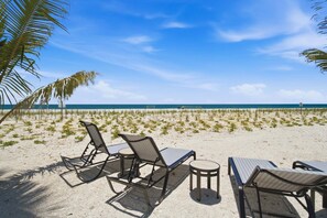 Ein Strand mit Liegestühlen und Tischen, Palmen und blauem Himmel.