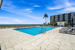 Piscina com vista clara para o oceano, rodeada por espreguiçadeiras e um edifício de design moderno.
