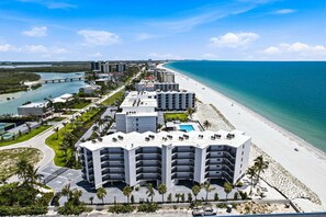 A multi-story hotel with a pool, located near a beach and a waterway. - Beachfront 2BR Condo with Gulf Views, Screened Lanai & Pickleball | Sleeps 4 (Bonita Springs)