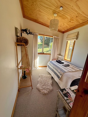 A bedroom with a bed, a wooden ladder, a window, and a ceiling light fixture.