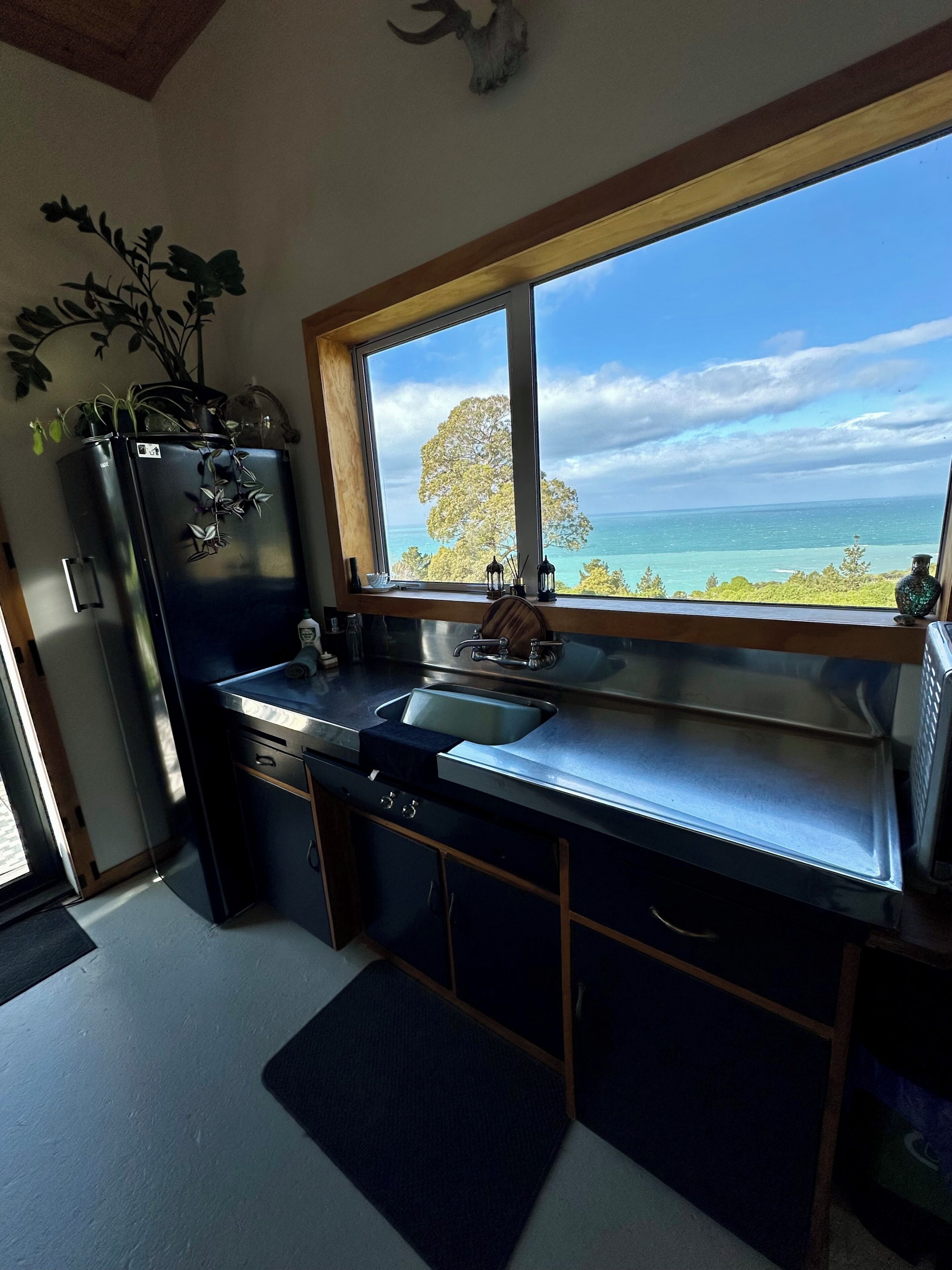 A kitchen with a view of the ocean, a refrigerator, a sink, and a window.