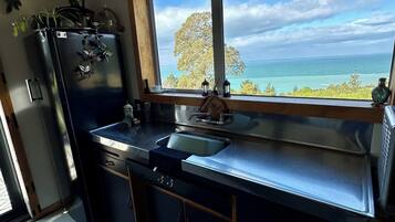 A kitchen with a view of the ocean, a refrigerator, a sink, and a window.