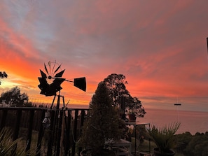 A windmill silhouette against a sunset sky, with a view of the sea and vegetation.