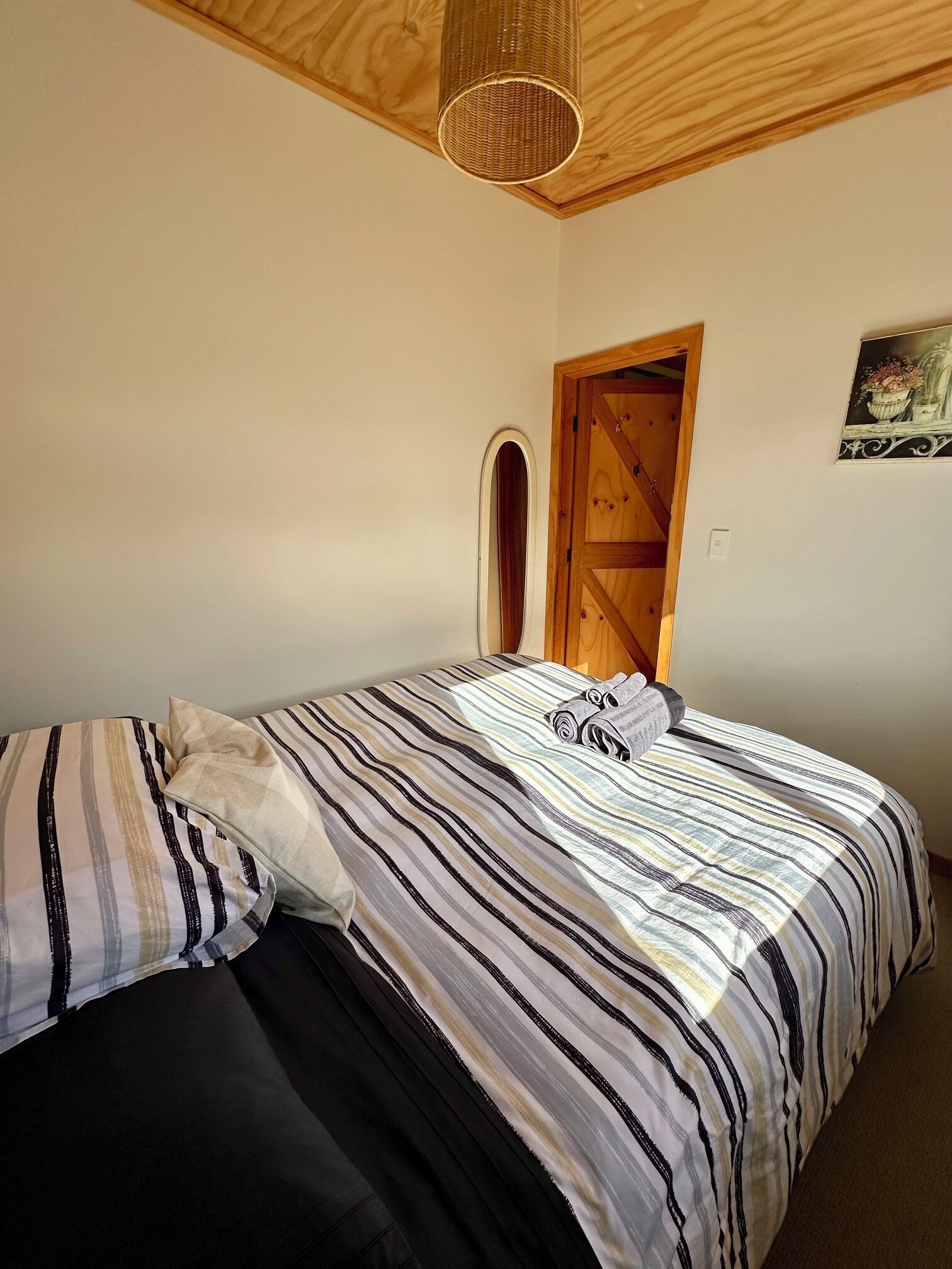 Ein Schlafzimmer mit einem Bett, Kissen, einer Holztür und einer Pendelleuchte.