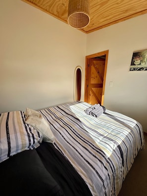 A bedroom with a bed, pillows, a wooden door, and a hanging light fixture.