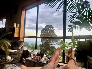 A room with a large window, a wicker chair, a small table with bottles, and a view of a tree and sky. - Bang for your buck, Sanctuary, Sea & Starry nights, 5 minutes from Gore Bay! (Domett)