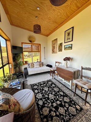 A cozy room with a bed, a dining table, chairs, a large window, and artwork on the walls.
