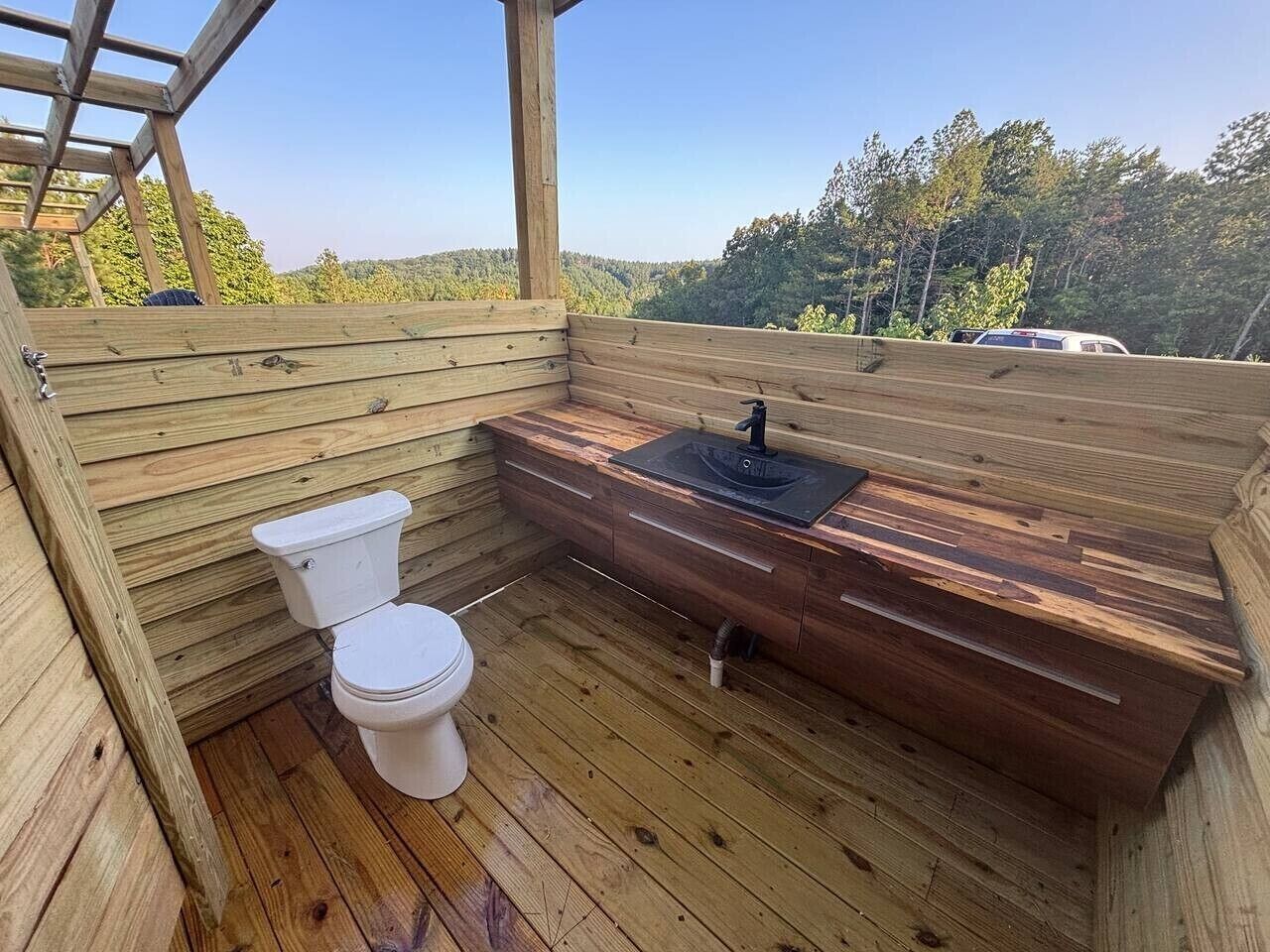 A wooden deck with a toilet and sink, surrounded by a wooden cabin structure.