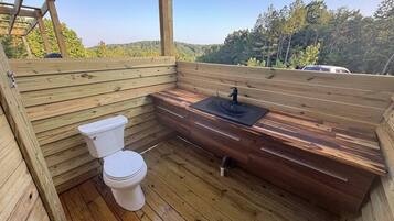 A wooden deck with a toilet and sink, surrounded by a wooden cabin structure.