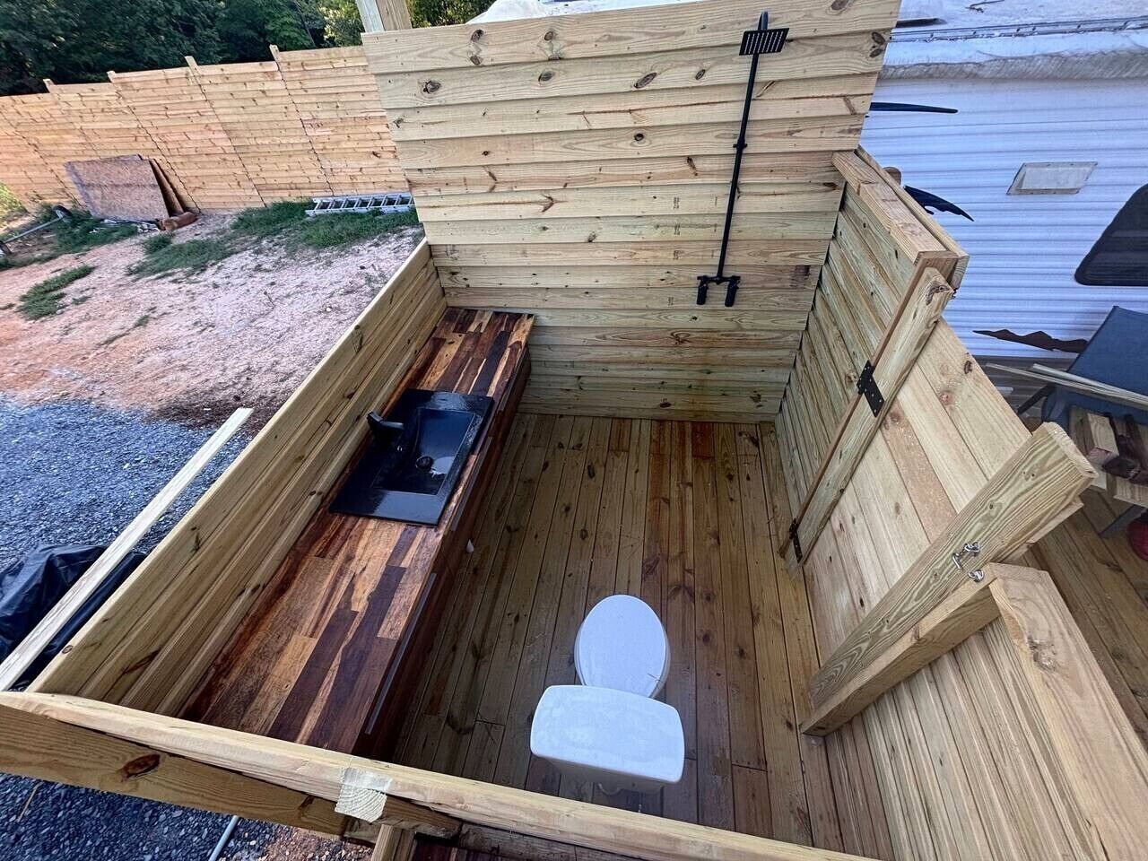 A wooden outdoor toilet with a bench and a black metal structure.