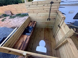 Et træ-toilet udendørs med bænk og en sort metalstruktur.