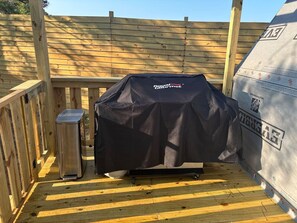 Una parrilla con cubierta negra, un cubo de basura y una terraza de madera.