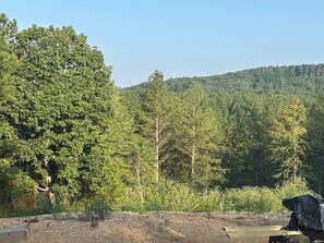 Un camping con un árbol grande al frente, una zona de grava y una colina boscosa al fondo.