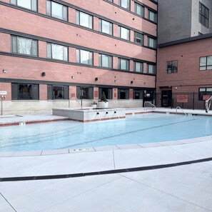 Ein Schwimmbecken mit Fliesen umgeben, umgeben von einem mehrstöckigen Gebäude mit großen Fenstern und einer Ziegel Fassade.
