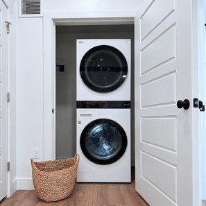 A laundry room with two stacked washing machines, a basket, and a door. - Downtown SLC Studio | King Bed + Free Parking (Salt Lake City)