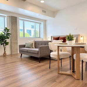 A modern living room with a grey sofa, a round wooden coffee table, and a potted plant. - Downtown SLC Studio | King Bed + Free Parking (Salt Lake City)