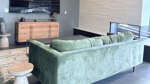 Una sala moderna con un sofá verde, un aparador de madera y un televisor de pantalla plana grande montado en la pared.