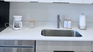 Una cocina moderna con armarios blancos, un lavamanos de acero inoxidable, una cafetera y algunos artículos de aseo sobre la encimera.