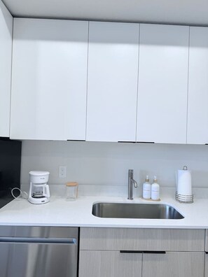 Eine moderne Küche mit weißen Schränken, einer Spüle aus Edelstahl, einer Kaffeemaschine und einigen Pflegeprodukten auf der Arbeitsplatte.