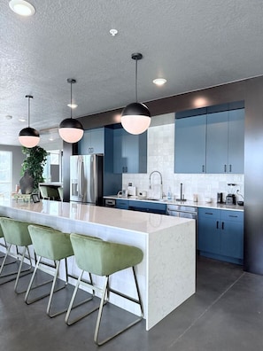 A modern kitchen with a central island, bar stools, and blue cabinets. - Downtown SLC Studio | King Bed + Work Space (Salt Lake City)