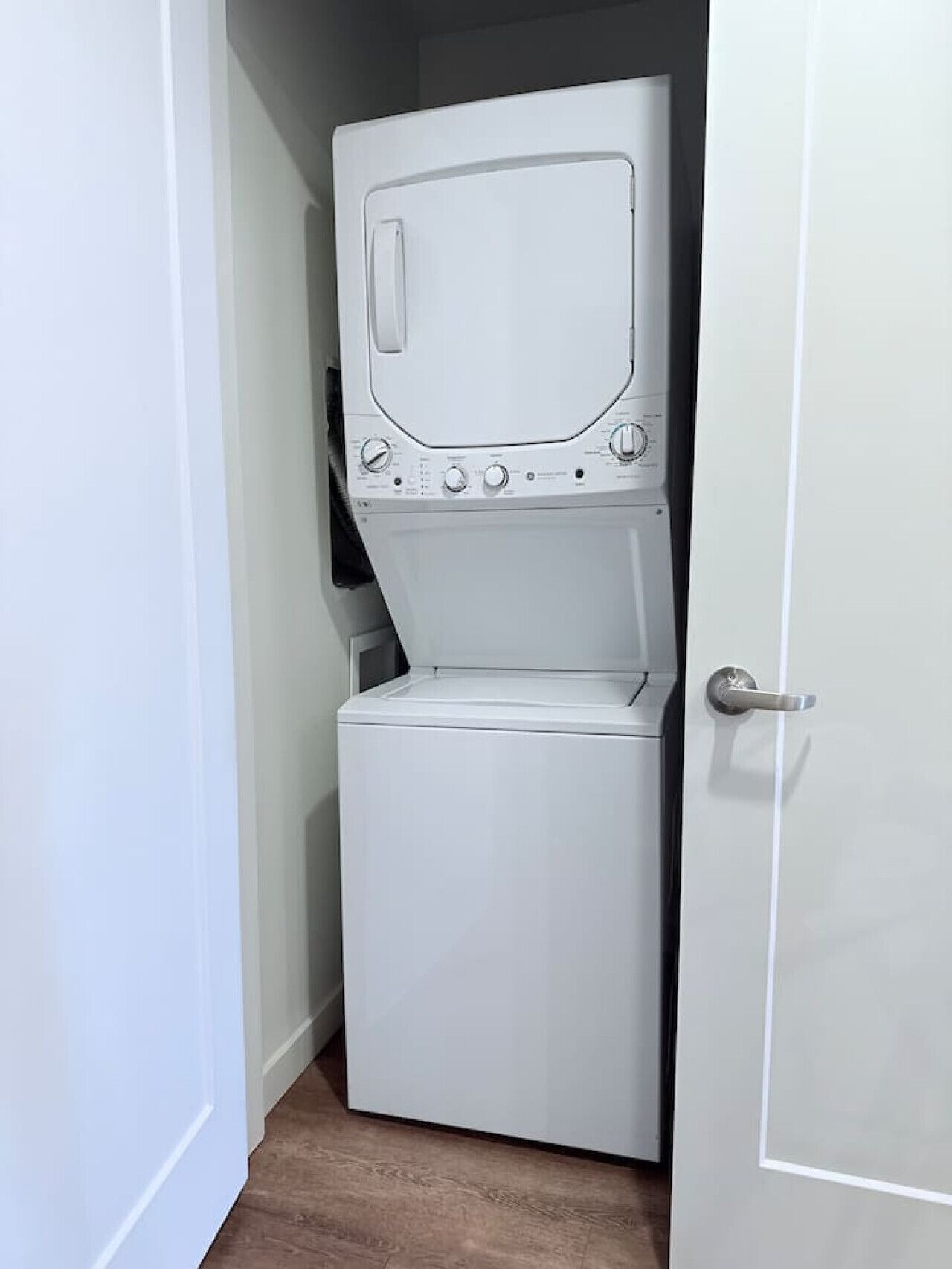 A compact, white laundry room with a front-loading washer and dryer, a door handle, and a small window.