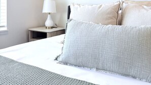 Un dormitorio con cama, almohadas, una mesita de noche, una lámpara y dos obras de arte colgadas en la pared.