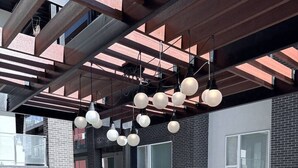 Un espacio de descanso al aire libre con mobiliario blanco, pared de ladrillo y luces esféricas colgantes.