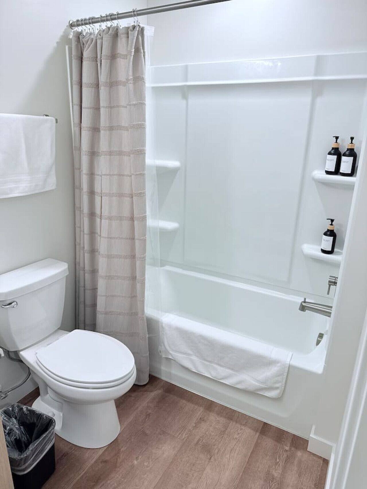 Une salle de bain avec des toilettes, une douche et une baignoire. Il y a deux bouteilles sur une étagère.