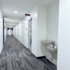 Ein Hotelgang mit einem Fitnesscenter-Schild, einer Glastür und einem Waschbecken mit Handtuchspender.