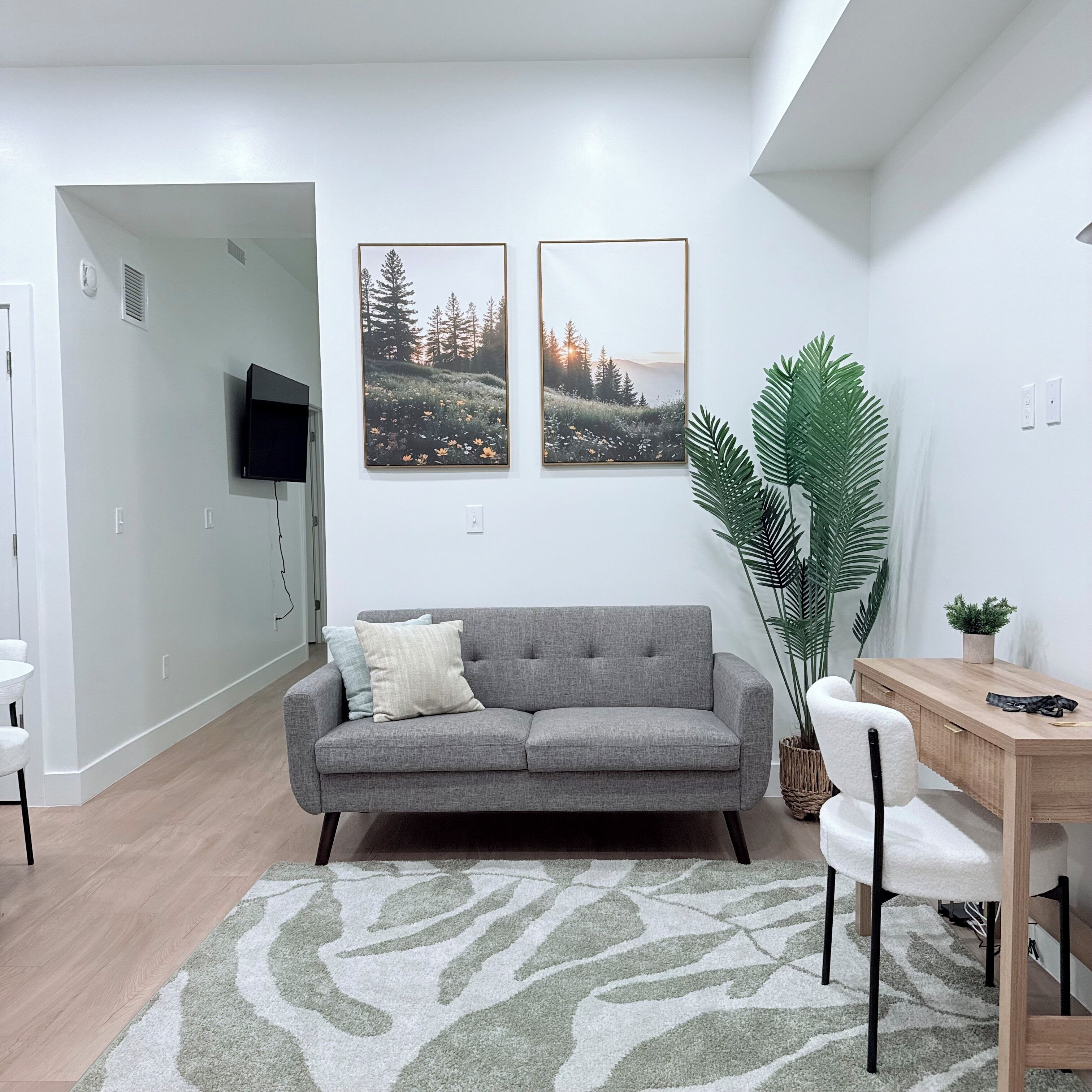 Ein modernes Wohnzimmer mit grauem Sofa, einem Couchtisch, einem an der Wand befestigten Fernseher und zwei gerahmten Landschaftsbildern.