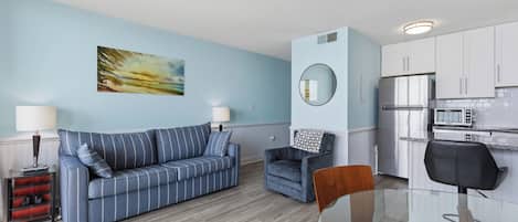 Un espacio habitable compacto con sofá, sillón, mesa de comedor y kitchenette.