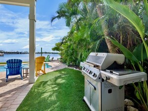 A patio with a grill, a pool, and chairs. - The Bayfront - Bayfront Pool Spa by Anna Maria Life Vacation Rentals (Bradenton Beach)