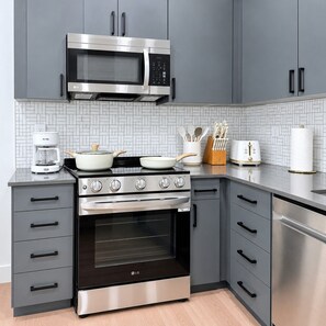 A modern kitchen with grey cabinetry, a stainless steel microwave, a coffee maker, a stove, and a toaster. - Luxury Downtown SLC Studio | King Bed + Parking (Salt Lake City)
