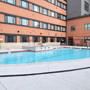 A swimming pool with a tiled deck, surrounded by a brick building with multiple windows. - Luxury Downtown SLC Studio | King Bed + Parking (Salt Lake City)
