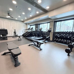 Un gimnasio con cintas de correr, una banca y mancuernas.