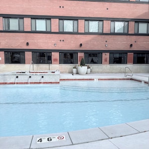 Piscina contigua a un edificio de fachada de ladrillo, con ventanas amplias y un letrero que indica las normas de la piscina.
