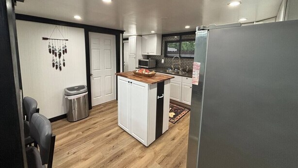 Una cocina compacta con una isla central, armarios blancos, microondas y refrigerador.